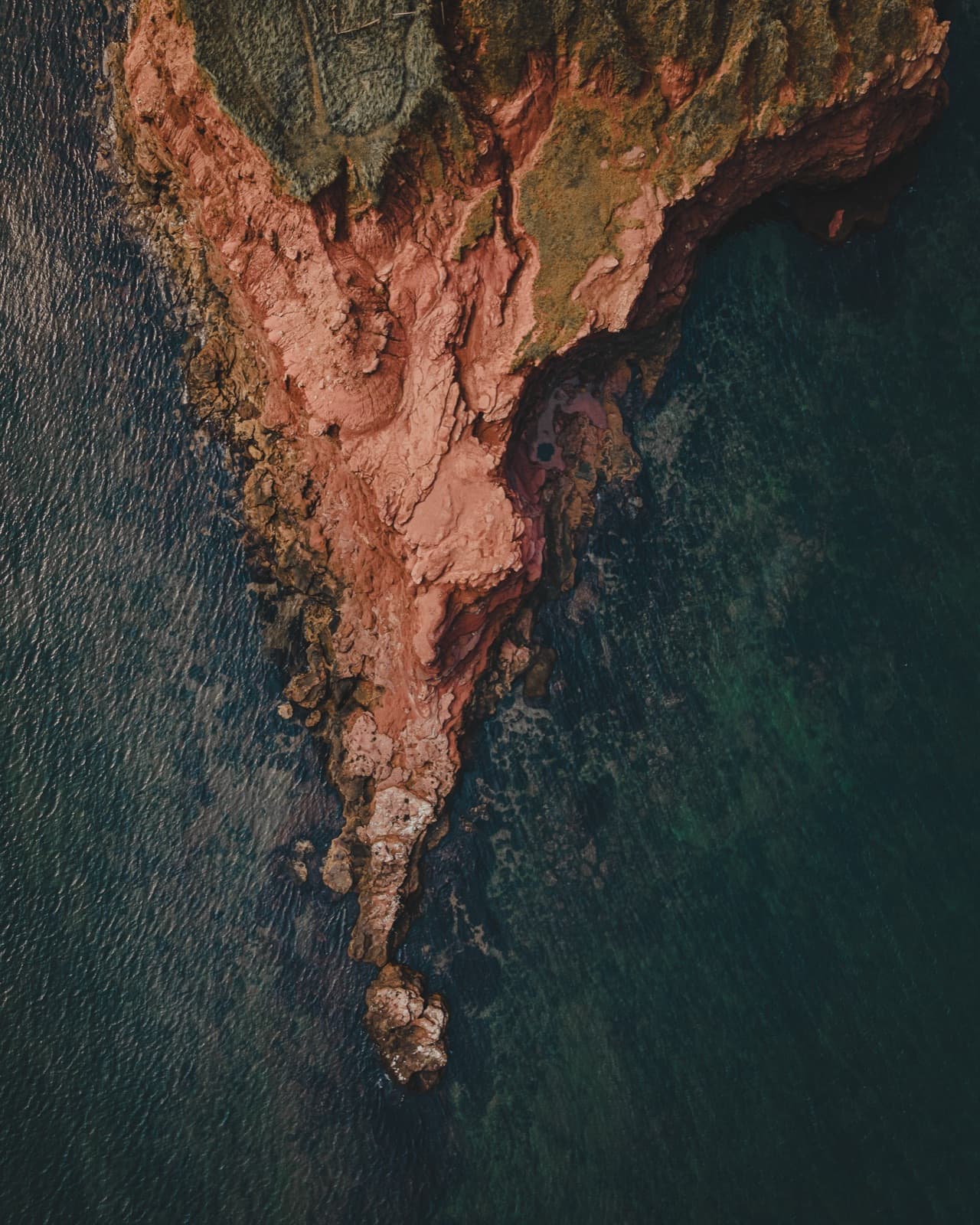 Aerial photograph of red cliff peninsula in dark water