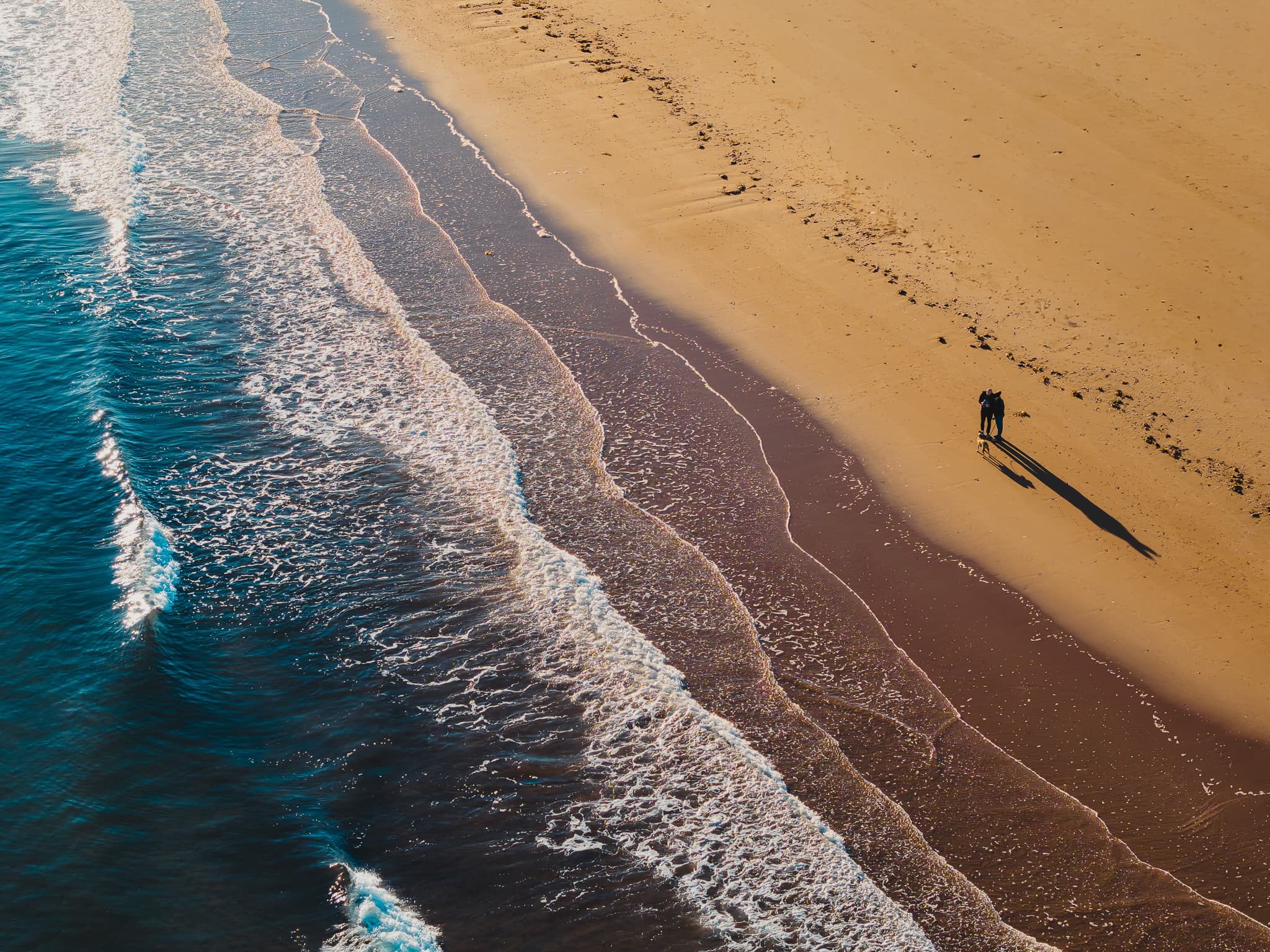 Aerial of two figures walking on an empty beach
