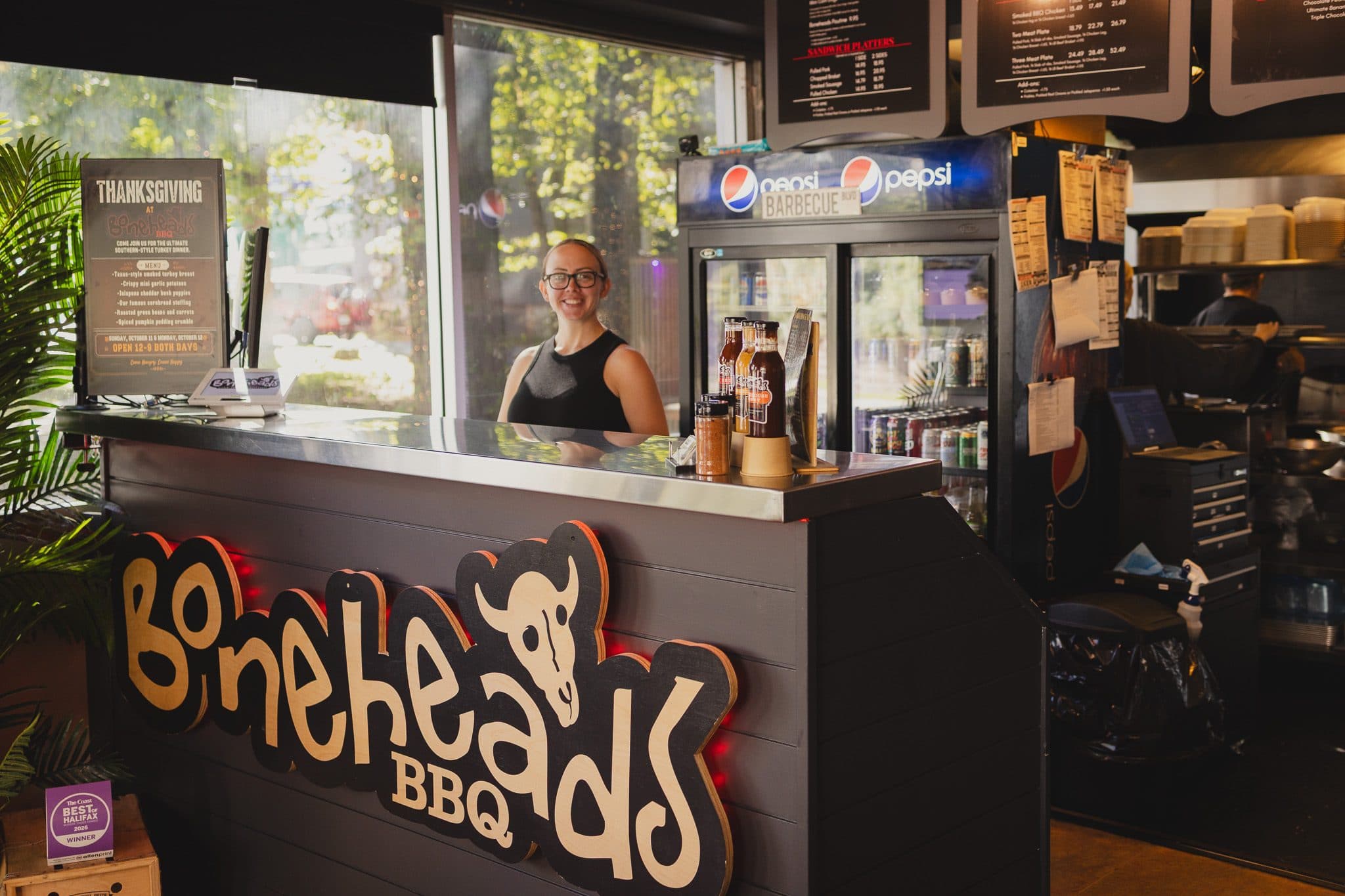 The order counter at Boneheads BBQ, a crew member smiling behind it, sauce bottles on the counter