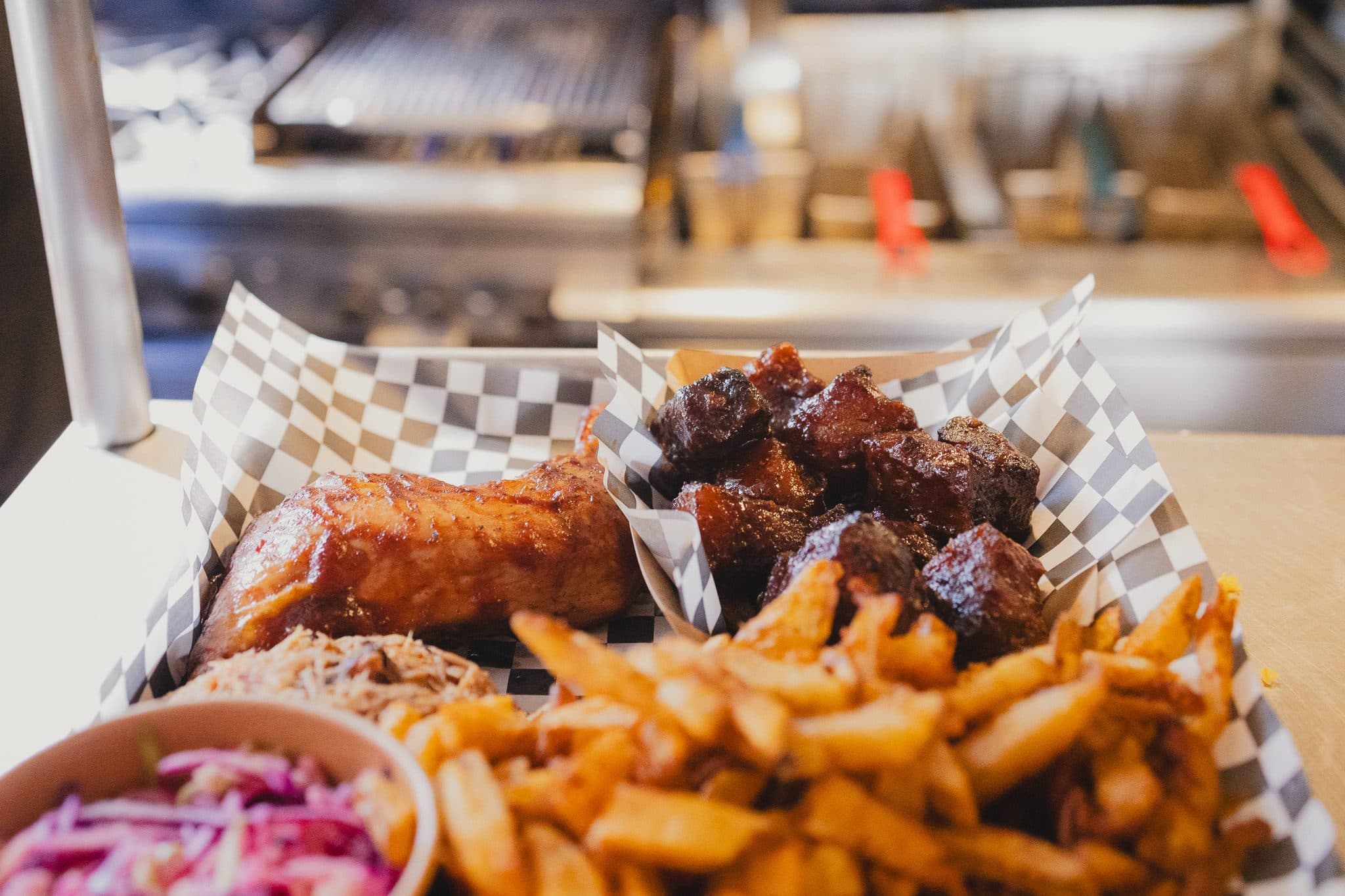 A meat plate at the pass: ribs, burnt ends, pulled pork, fries, and purple slaw on checkered paper